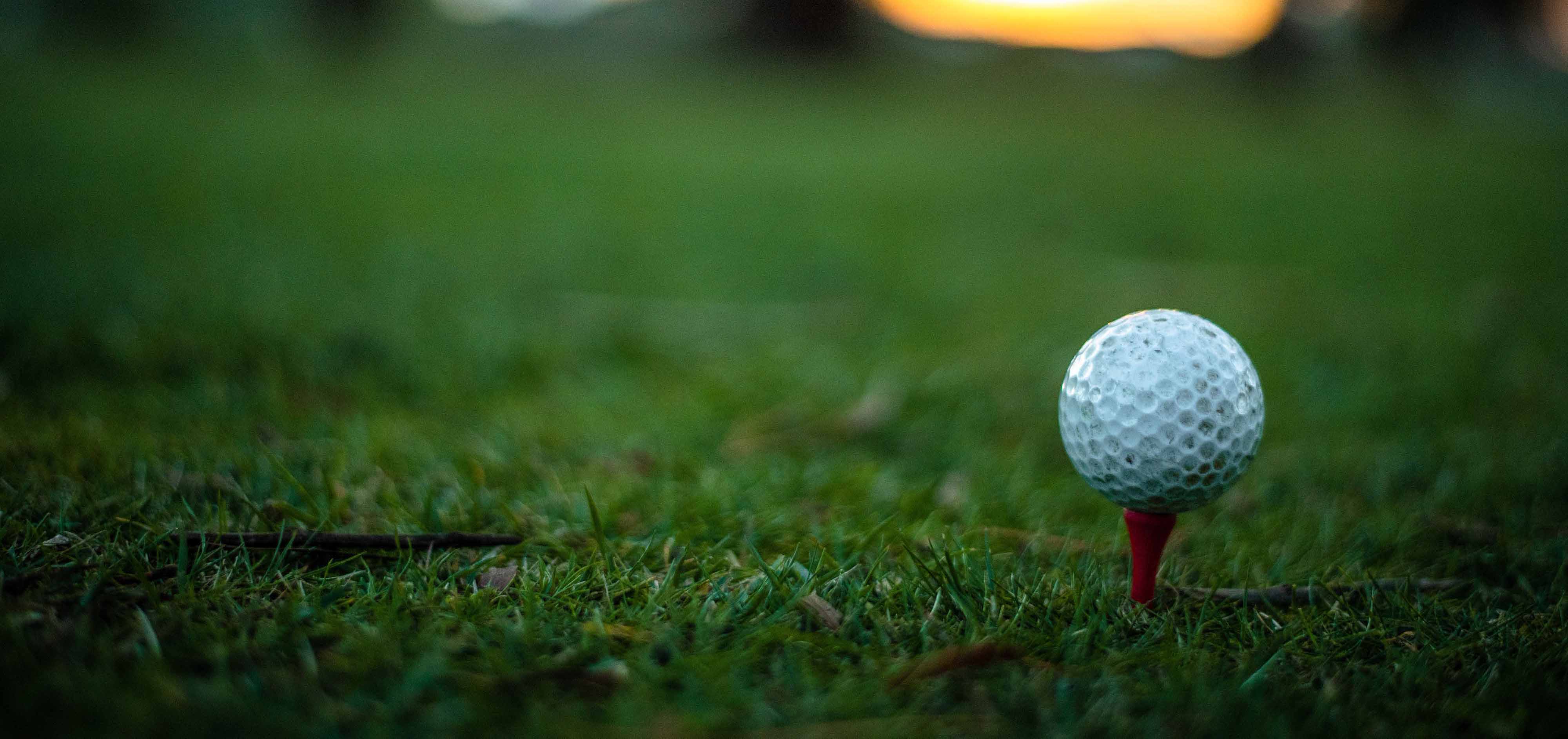 An image of a golf ball sitting on a tee that in placed in the ground on a golf course.